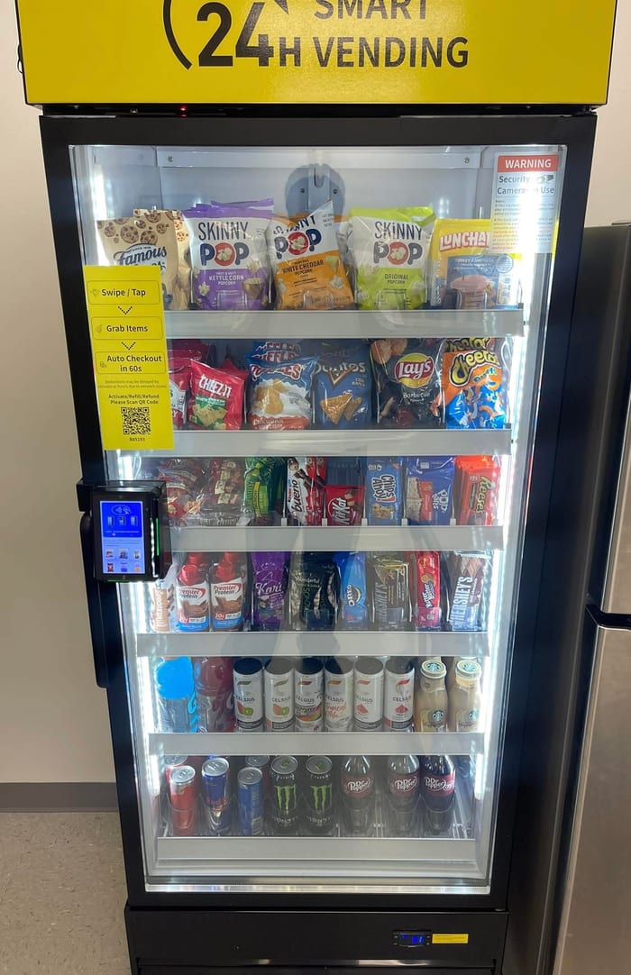 Yellow-header managed micro market unit stocked snack-forward with SkinnyPop kettle corn, Cheez-It, Doritos, Lays, Cheetos, Snickers, Reese's, and Hershey's bars.