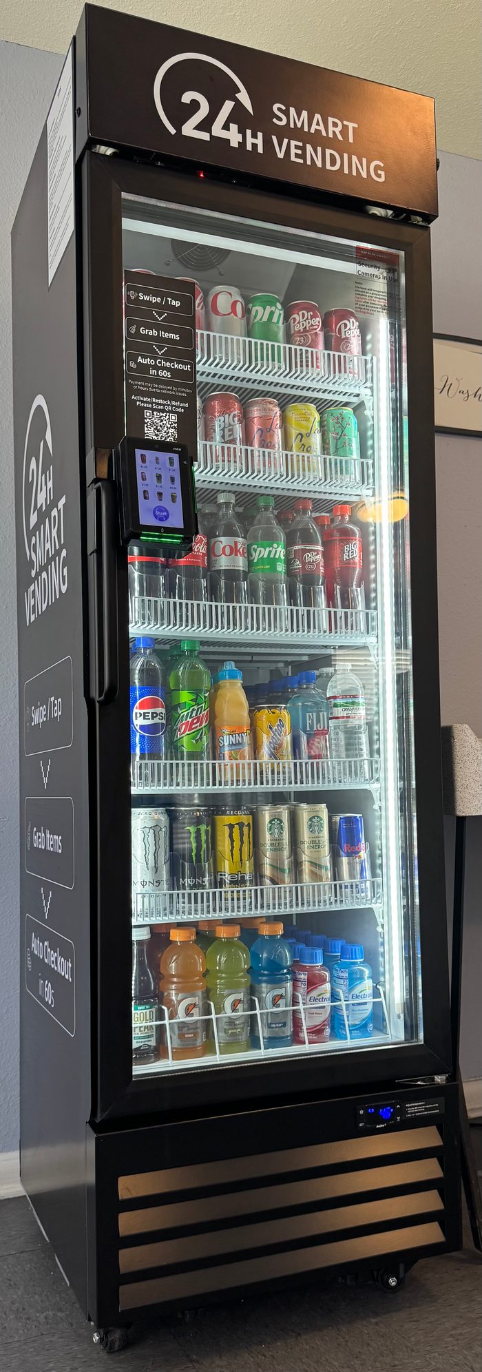 Three-quarter view of an installed managed micro market showing the side panel, the front glass with stocked product, and the tap-to-pay screen.
